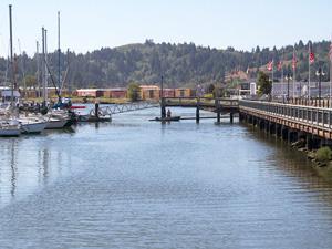Coos Bay's boardwalk is on the right side of the image and a row of boats are tied to a dock on the left side of the image