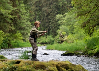 A fly-anglers stands on a huge boulder casting into Drift Creek.