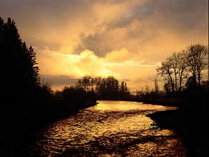 A yellow-orange sunrise illuminates a stretch of the Wallowa River.