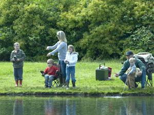 a family stands on the bank of Alton Baker Canoe Canal with fishing lines in the water and a cooler behind them