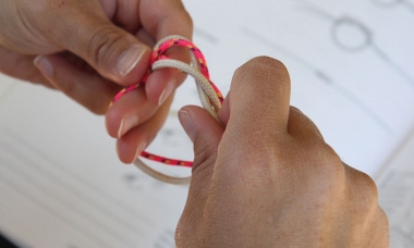 a person is practicing tying knots. A knot tying book is out of focus in the background