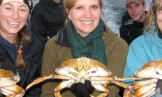 photo of three smiling women each holding a Dungeness crab