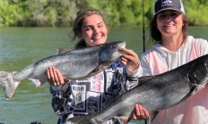 Two smiling female anglers each hold up a recently caught Chinook salmon