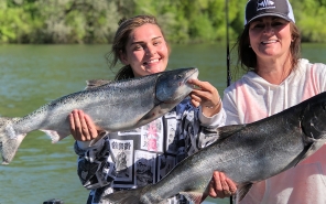Two smiling female anglers each hold up a recently caught Chinook salmon