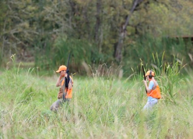 Two hunters walking through tall grass field