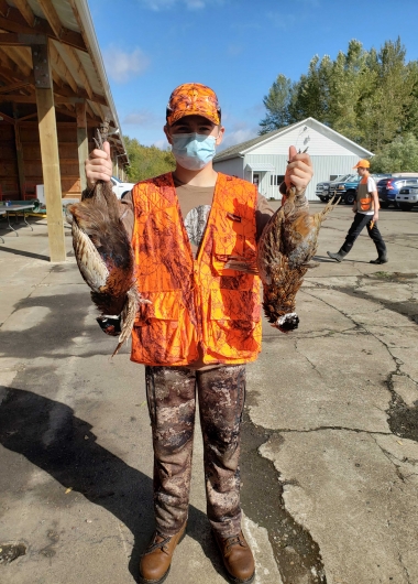 young hunter holding up two harvested pheasants