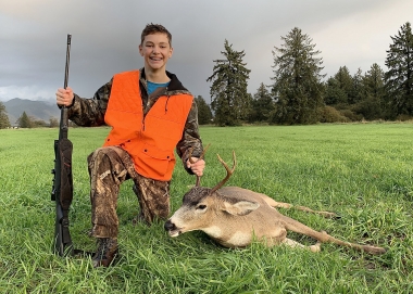Young hunter with a black-tailed deer in a grassy field.