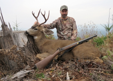 Hunter and his deer in a clear-cut field, posing with a muzzleloader.