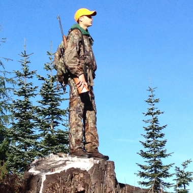 A young rifle hunter standing on a stump for a bird's eye view of his hunt unit.