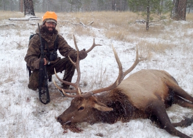 Hunter with a big buck elk in a snowy field.