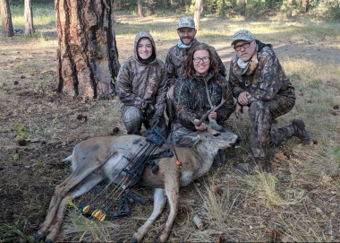 A successful mule deer hunter and her deer with several supportive family members
