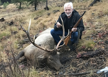 A rifle hunter poses with a Rocky Mtn elk in the open terrain of the Sled Springs Unit.