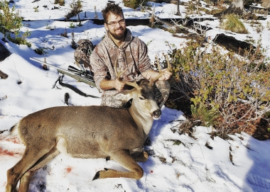 Hunter in a open snowy filed with a fine black-tailed buck deer. 