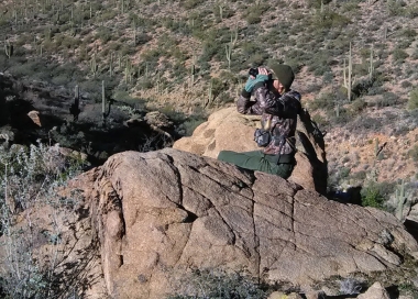 Hunter perched on a boulder glassing for elk.