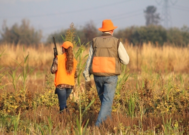 A young hunter walks in a grassy field with an adult mentor nearby