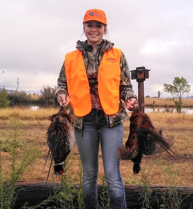 Young hunter in orange cap and vest holds two recently harvested pheasants