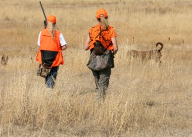 Two young hunters with a dog walk in grassy field away from camers