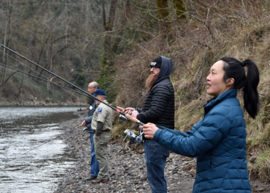 Four anglers stand on a rocky bank casting into river