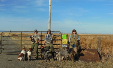 Three female hunters with their dogs, holding pheasants in front of access sign