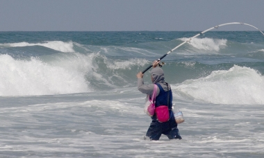 angler in the ocean surf casting for surfperch