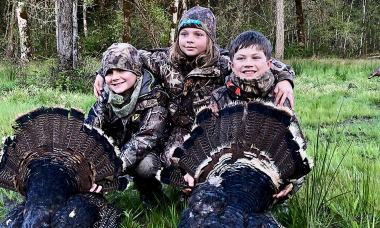 Three young hunters pose with two harvested turkeys