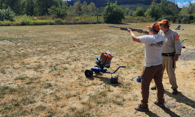 Shooter aiming a shotgun while instructor looks on