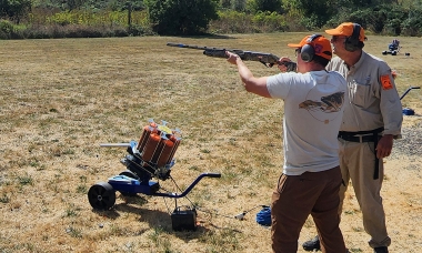 Shooter aiming a shotgun while instructor looks on