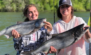 Two smiling female anglers each hold up a recently caught Chinook salmon