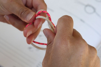 a person is practicing tying knots. A knot tying book is out of focus in the background