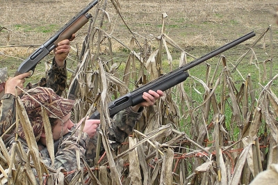 Two hunters in a blind taking aim at some flying birds.