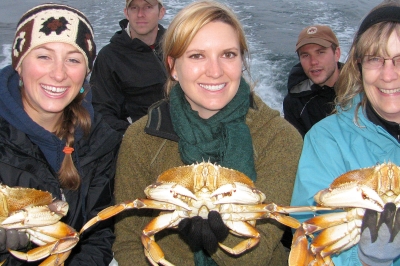 Three smiling women hold Dungeness crab