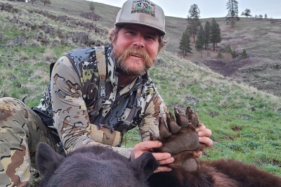 Hunter in camo clothing holds up the paw of a large black bear