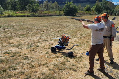 Shooter aiming a shotgun while instructor looks on