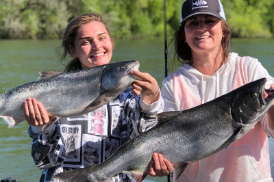 Two smiling female anglers each hold up a recently caught Chinook salmon