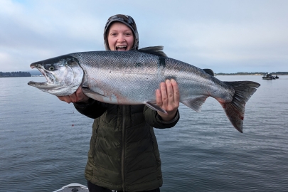 Smiling anglers holds out a large Chinook with both hands