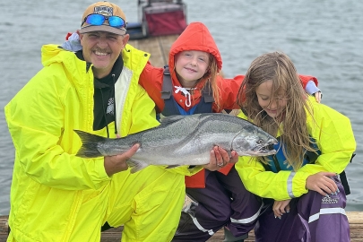 An adult male and two young girls, all in bright raingear, pose with a coho salmon